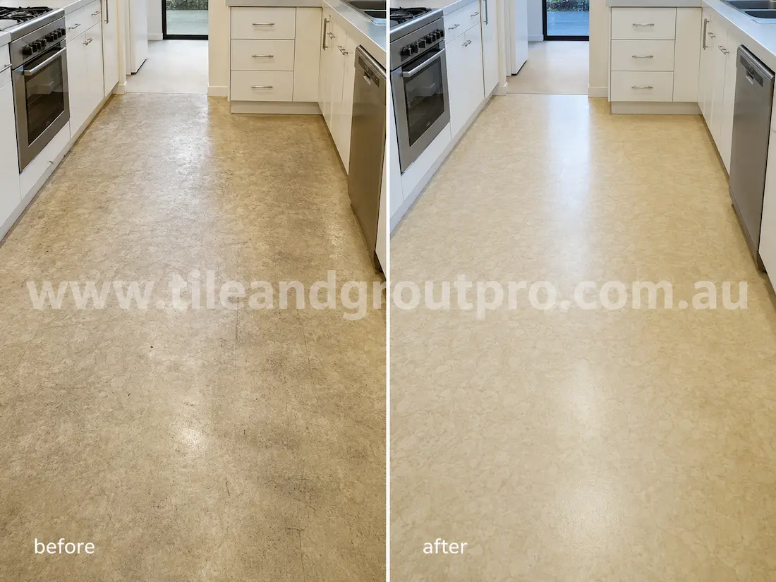 Residential kitchen with beige linoleum floors before sealer stripping, displaying dark traffic stains, faded sealer, scuff marks, and uneven surface wear between cabinets and appliances.