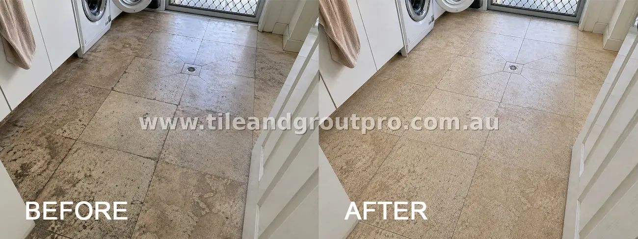 Natural stone laundry floor tiles around a drain with visible grime, moisture staining, and dirty grout lines before tile and grout cleaning