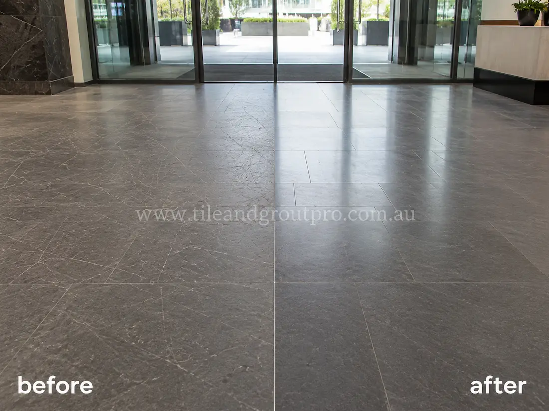 Commercial building lobby with large dark bluestone floor tiles before and after scratch removal, showing scratched and worn stone tile surfaces restored to a clean professional finish near glass entry doors.