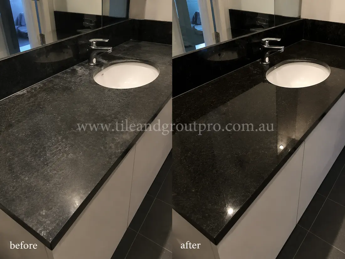 Before tile renewal, the black granite bathroom vanity countertop had water marks, soap residue, and a faded finish around the sink and mirror area.