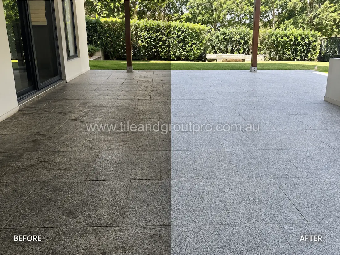 Outdoor granite patio pavers before grinding, displaying weathered dark stone tiles, surface staining, and faded finish under the covered alfresco area.