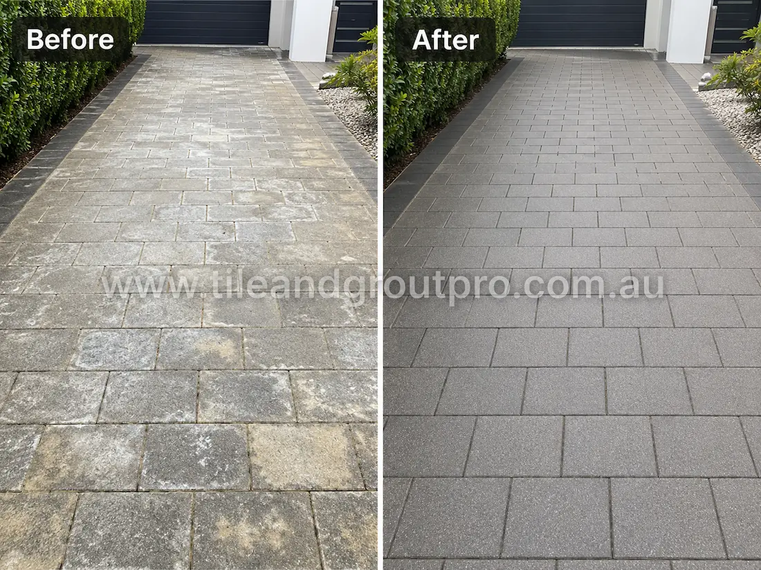 Residential driveway with grey concrete pavers before sealer stripping, showing white sealer haze, patchy residue, and faded surface finish bordered by hedges and garden edging.