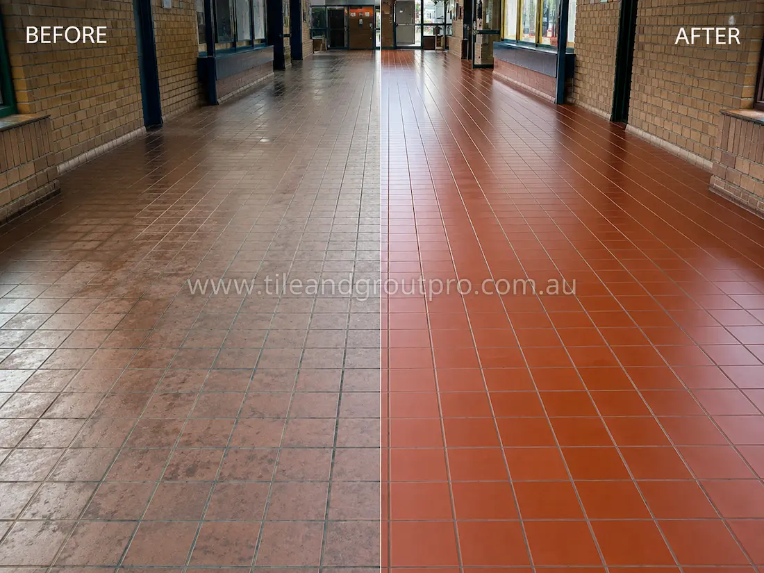 Before tile renewal, red quarry floor tiles in a school atrium corridor showed heavy foot-traffic wear, dull surfaces, embedded dirt, and faded grout lines in a large educational walkway.