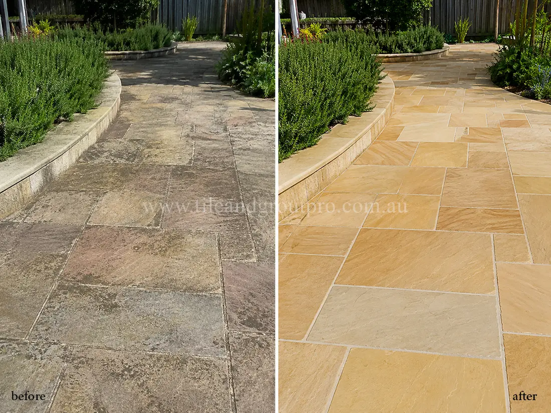 Before tile renewal, sandstone garden pathway tiles showed weather damage, dark staining, and worn natural stone surfaces along a landscaped outdoor walkway bordered by greenery.