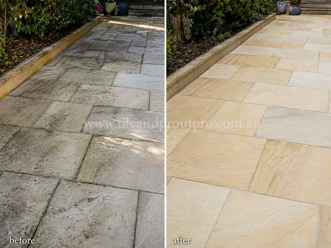Before tile renewal, sandstone garden walkway tiles showed dark staining, dirt buildup, and weathered natural stone surfaces along an outdoor residential pathway bordered by raised garden beds and shrubs.