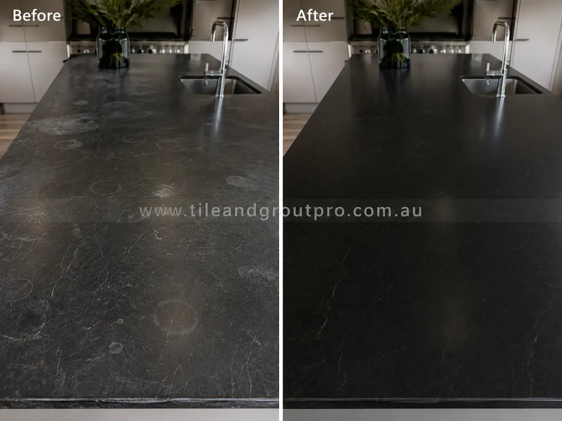 Black soapstone kitchen island countertop with visible ring stains, scratches, and dull etched areas before professional grinding and refinishing.