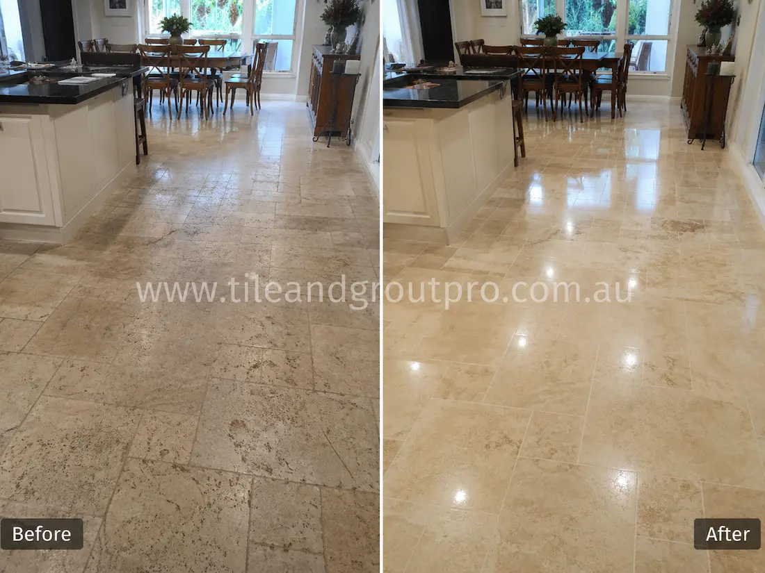 Kitchen and dining area travertine tile floor before grinding, featuring heavy etching, dull traffic paths, surface scratches, and worn stone finish throughout the open interior space.